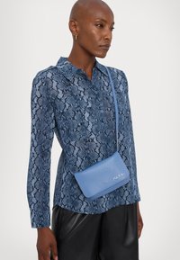 Kvinne iført en blå skjorte med slangeskinnmønster, svarte skinnbukser og en liten lyseblå crossbody-veske med "Marni"-logo.