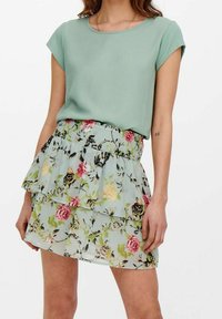 Haut vert clair à manches courtes associé à une jupe à motifs floraux superposés avec des roses roses et jaunes sur un fond menthe.