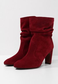 Botines de ante rojo con un diseño arrugado, punta afilada y un tacón de altura media. Textura suave sin hardware o patrones visibles.