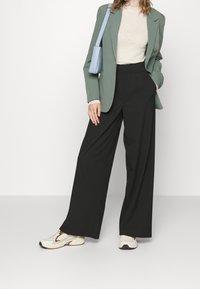 Green blazer, beige top, wide black pants, and white sneakers. The blazer has a structured design, while the pants are loose-fitting.