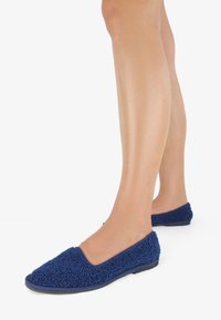 Scarpe slip-on blu navy realizzate con un materiale morbido, testurizzato e peloso. Presentano una punta arrotondata e una suola in gomma flessibile per il massimo comfort.