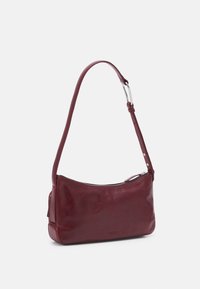 Sac à bandoulière en cuir bordeaux avec un design incurvé, quincaillerie en argent et fermeture éclair. Dispose d'une sangle réglable et d'une texture lisse.
