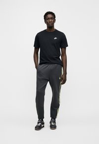 Maglietta Nike nera con logo, pantaloni da jogging grigi con strisce verdi e marchio, e scarpe sportive nere con dettagli bianchi.