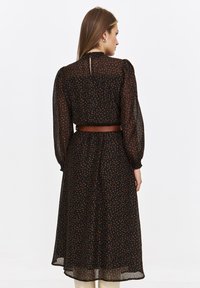 Czarna sukienka w kropki z wysoką szyją i bufiastymi rękawami. Posiada pasek w talii i detal w postaci otworu na plecach. Wykonana z lekkiego materiału.