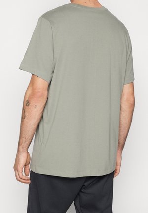 Man wearing plain light gray short-sleeve t-shirt and black pants, shown from the back with visible arm tattoos.