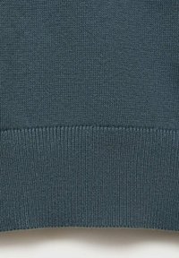 Knitted sweater in dark teal with a ribbed hem. Smooth texture with a consistent pattern of stitches throughout the fabric.