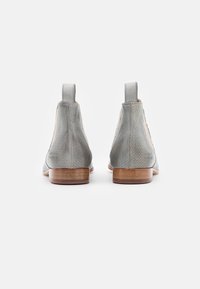Botas de tobillo de cuero gris con textura perforada, paneles laterales elásticos y un tacón de madera. Diseño suave, punta redondeada, estilo minimalista.