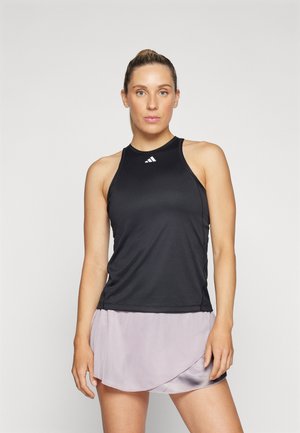 Débardeur de sport noir avec un col rond et un dos nageur, associé à une jupe style enveloppant de couleur violet clair. Tissu doux, peu de marquage.