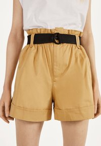 Tan shorts made of smooth fabric, featuring a cinched waistband with a black belt. The hem is cuffed for a tailored appearance.