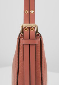 Struktureret taske i teksturede, koralfarvede læder med dobbelte smalle stropper. Udrustet med guldfarvet hardware og sorte detaljer langs sømmene.