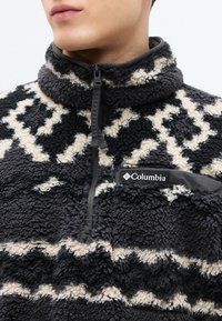 Φλις μπλουζάκι σε μαύρο και κρεμ με σχέδιο, με φερμουάρ στον λαιμό, υφή στην επιφάνεια και λογότυπο Columbia στην τσέπη στο στήθος.