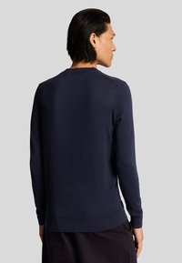Maglione blu navy, realizzato in morbido tessuto a maglia, presenta maniche lunghe, collo tondo e orlo aderente. Tessuto liscio con dettagli minimi.