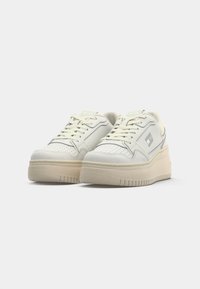 Weiße Leder-Sneaker mit einer dicken cremfarbenen Sohle, durchlöchertem Zehenbereich und minimalistischem silbernen Logo. Die Schnürsenkel und der gepolsterte Schaft erhöhen den Komfort.