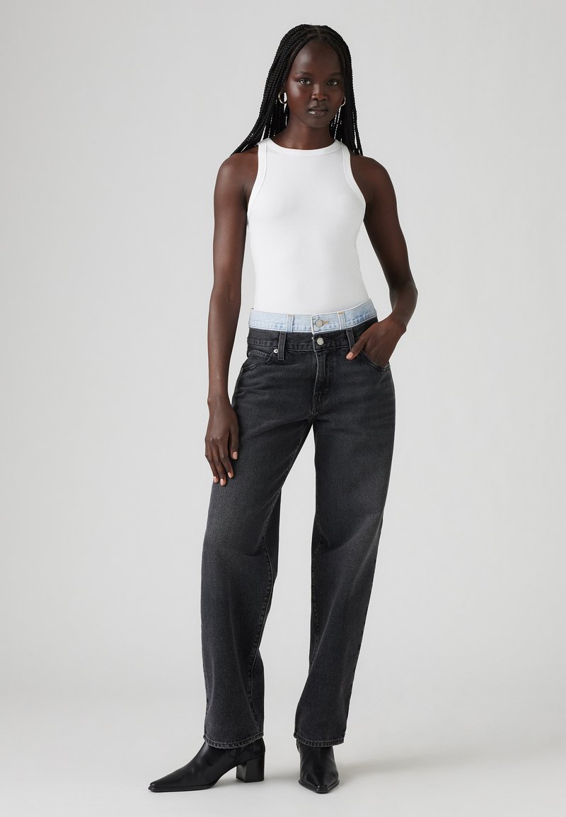 Jean noir taille haute à jambe large avec une ceinture en denim bleu clair, associé à un haut sans manches blanc et des bottines noires à talons pointus.