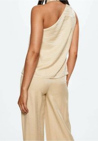 Haut beige à une épaule en tissu léger et brillant, associé à un pantalon large assorti, tous deux présentant une texture lisse et une coupe décontractée.