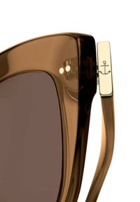 Bruine oversized zonnebril met een glanzende afwerking. De poot heeft een klein gouden anker embleem. Donker getinte glazen bieden bescherming.