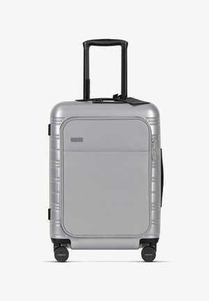 Zilveren harde koffer met een uitschuifbare handgreep, dubbele wielen, een voorvak met rits en gegoten accenten langs de zijkanten.