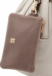 Bolso de cuero gris con un bolsillo con cremallera de cuero marrón desmontable, herrajes dorados, textura suave y detalle del logotipo en relieve en el bolsillo.