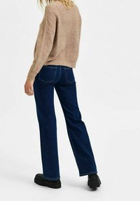 Maglione beige in maglia con texture a coste, abbinato a jeans dritti blu scuro e stivali neri con plateau, visto da dietro.