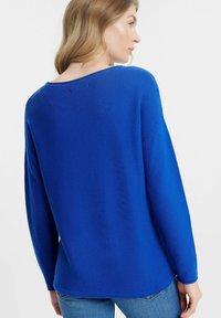 Maglione blu lavorato a maglia con scollatura ampia e spalle ribassate, caratterizzato da una finitura testurizzata e un orlo posteriore leggermente più lungo.