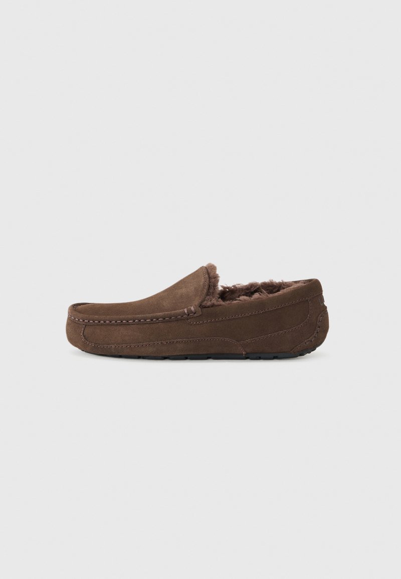 Chaussons en suède brun avec une doublure douce et duveteuse, un design à profil bas, et des détails de couture le long des bords. Pas de logos ou d'accents visibles.