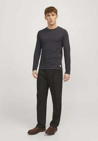 Camisa de manga larga gris oscuro con cuello redondo, combinada con pantalones negros y zapatos marrones. La camisa presenta una textura sutil y una etiqueta.