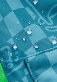 Des gouttes d'eau perlent sur un tissu imperméable bleu à motifs avec des coutures visibles et un bord de fond vert.