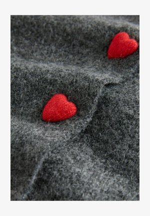 Gray wool fabric with two small red knitted hearts sewn on, creating a textured, cozy pattern.