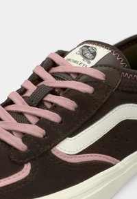 Καφέ αθλητικά παπούτσια από σουέντ με ροζ κορδόνια, λευκή ρίγα στο πλάι και χαρακτηριστικό λογότυπο. Διαθέτουν ραμμένα διακοσμητικά και υφασμένο πάνω μέρος.