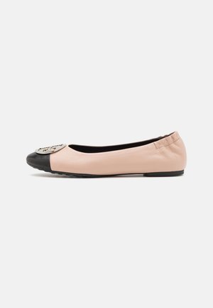 Bailarina de color rosa suave con puntera negra y emblema metálico redondo en la parte delantera, talón elástico y suela plana de goma negra.