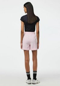 Rosa shorts med en texturerad design, elastisk midja och upprullade ärmavslut, i kombination med en svart åtsittande t-shirt och svarta randiga strumpor.