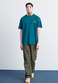Teal cotton t-shirt with a crew neckline, paired with olive cargo pants featuring side pockets, and orange and white sneakers.