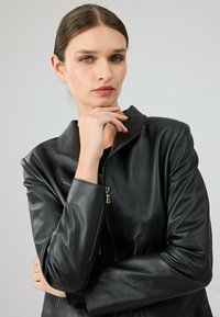 Giubbotto di pelle nera con chiusura a zip, colletto alto e una texture liscia. Dotato di maniche aderenti e taglio sartoriale.