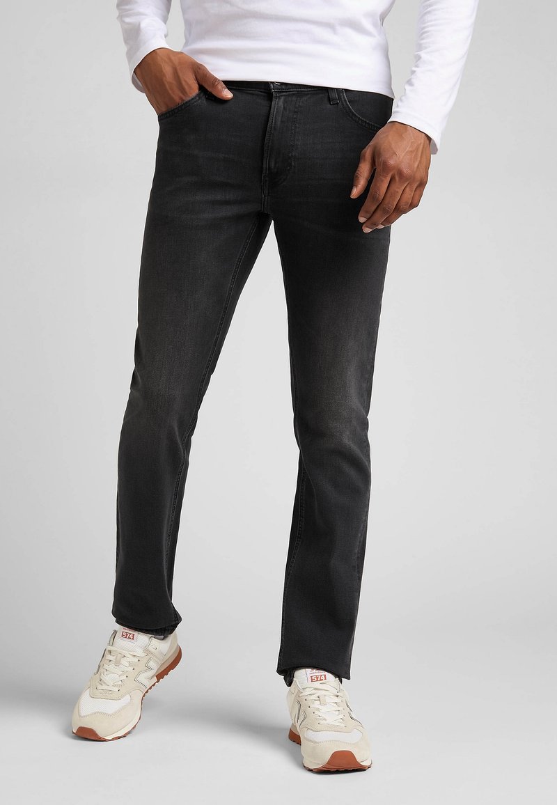 Zwarte denim jeans met een slim fit, vijf-pocket ontwerp en lichte vervaging. Gecombineerd met witte en beige sportsneakers.