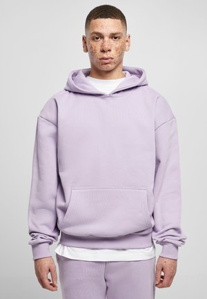 Light purple hoodie made of textured fabric. Features a kangaroo pocket, ribbed cuffs, and a relaxed fit. Worn over a white shirt.