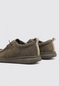 Scarpe in suede marrone con una forma arrotondata, accenti a strisce contrastanti sul tallone e una suola in gomma testurizzata. Dettagli di allacciatura sottili.