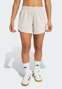 Licht beige sportshorts met een elastische tailleband, gestructureerde stof en licht uitlopende zoom. Gecombineerd met witte sokken en meerkleurige sneakers.