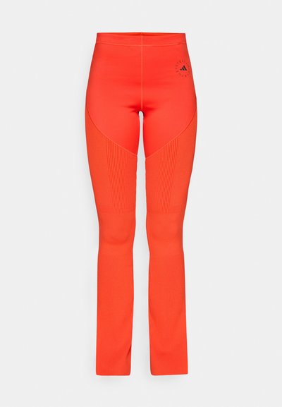 Ljust orange leggings med en åtsittande design, ruggade detaljer längs sidorna och en logotyp nära midjan. Slät textur genomgående.
