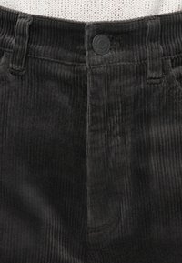Pantalons en velours côtelé noir avec une texture à côtes verticales, dotés d'une fermeture par bouton et de passants de ceinture au niveau de la taille. Aucuns autres détails visibles.