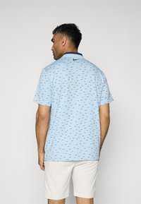 Light blue polo shirt made of smooth fabric with a collared neckline, featuring a subtle pattern of small dark blue icons and a black logo.