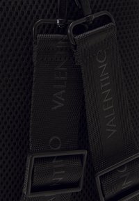 Black textured fabric featuring mesh material; adjustable straps with "VALENTINO" label; minimalistic design and black hardware accents.