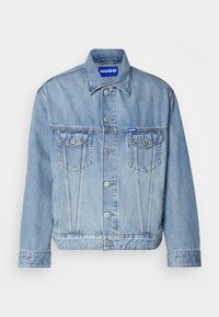 Light blue denim jacket with a button-up front, two chest pockets, and a branded blue patch on the upper left side. Classic collar and cuffs.