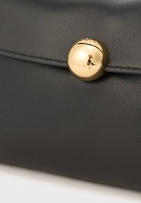 Sort lædertaske med en glat tekstur, der har en fremtrædende gylden cirkulær trykknap med præget "Furla."