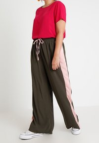Top rosa a maniche corte abbinato a pantaloni larghi verde oliva con una striscia rosa laterale. Abbinato a sneakers bianche.