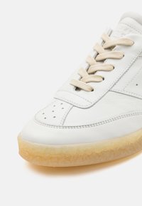 Baskets en cuir blanc avec lacets beiges, zone des orteils perforée, détails cousus et semelle en gomme translucide.