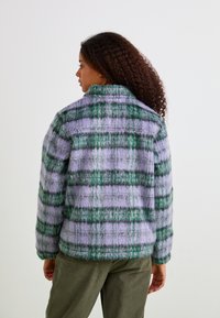 Fuzzy plaid jacket in purple and green with a collared neck. Features a relaxed fit and cozy texture, designed with visible stitching details.