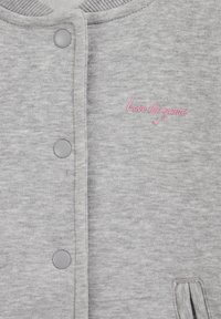 Šedá mikina s textúrovaným pletením, patentkami a ružovým vyšívaným nápisom „Love the game“ nad ľavým vreckom.