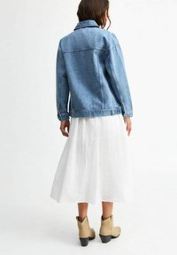 Giubbotto in denim azzurro chiaro con colletto classico, abbinato a una gonna bianca con motivi floreali e stivaletti beige con tacco largo.