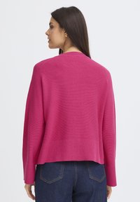 Pulover tricotat fucsia, cu o croială lejeră, textură cu nervuri și mâneci lungi. Are un gât rotund și o margine care se termină la talie.