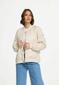 Gevoerde beige bomberjack met ribgebreide manchetten en zoom, voorzien van drukknoopsluiting en een logopatch op de linkermouw.